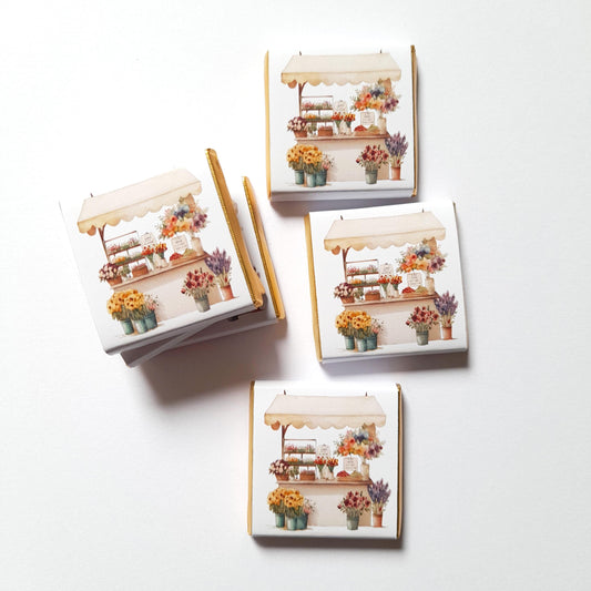 Flower market personalised chocolate favour – square Fairtrade milk chocolate (approx 3 × 3 cm, 5 g) wrapped in gold foil and glossy paper featuring a vibrant flower stall illustration, with customisable message on the back