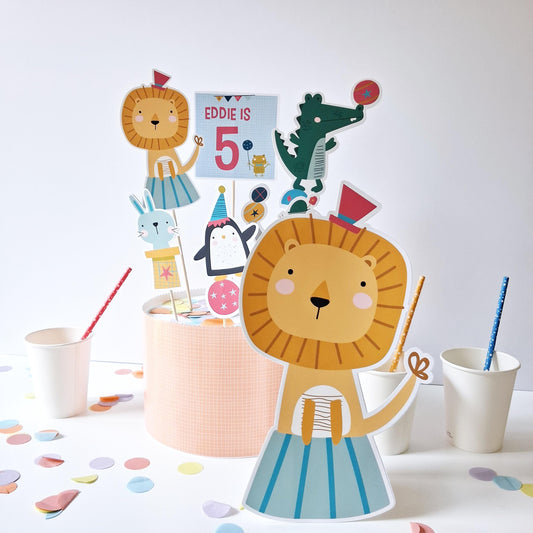 A personalized circus animal cake topper set for parties. Toppers for a lion, penguin, crocodile, elephant, and rabbit, plus a customizable name and age topper.