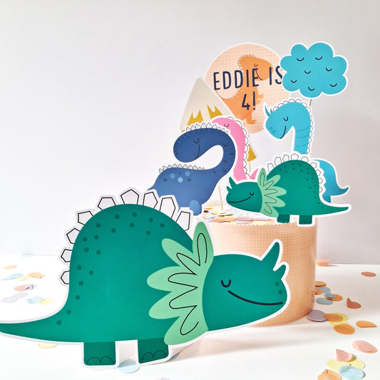 Handmade in the UK, this set includes a brachiosaurus, a triceratops, and a personalised name-and-age topper, along with a standing dino figure.