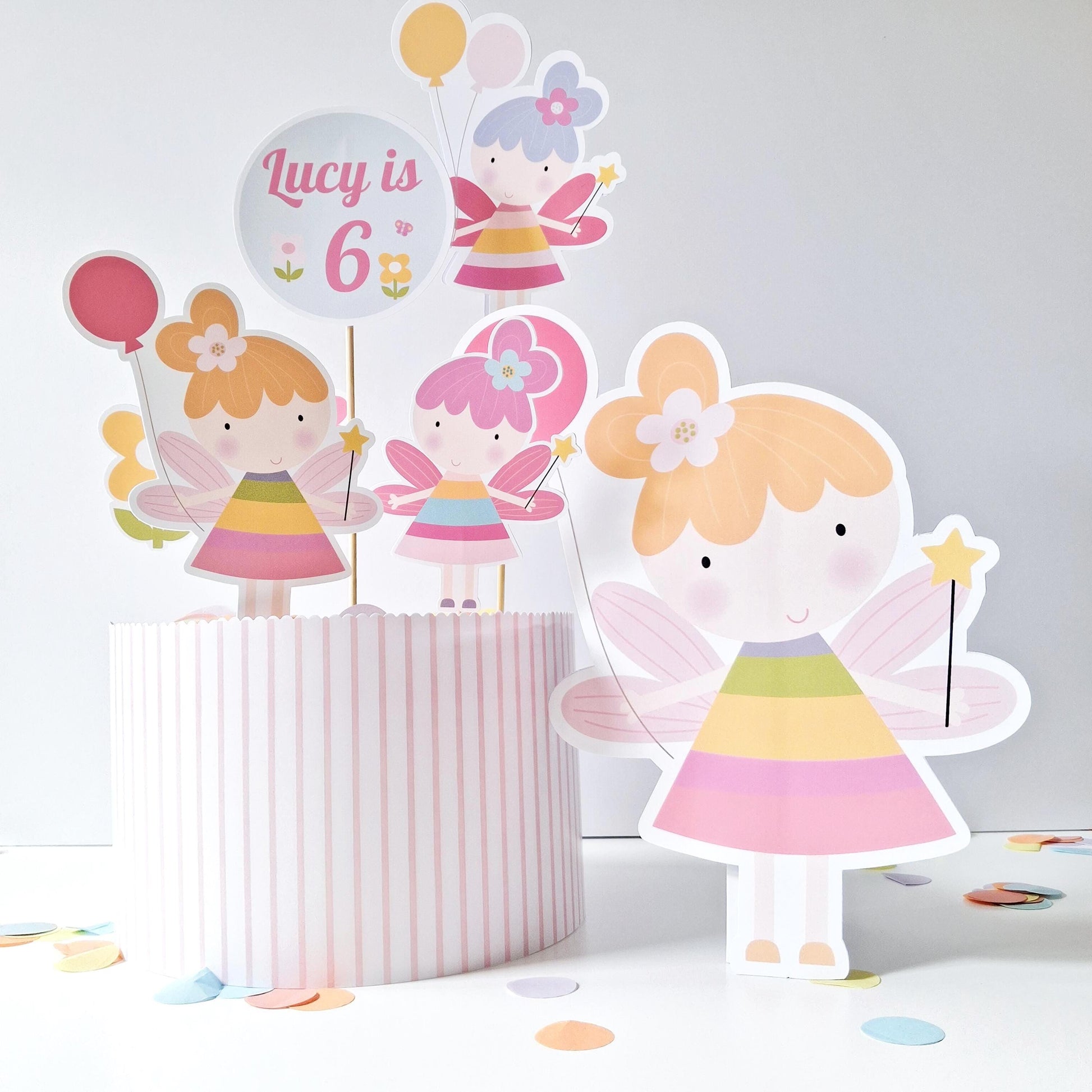 Magical Flower Fairy Cake Topper Set with Freestanding Figure. This set is designed to add a fairy-tale charm to a cake. It includes a freestanding fairy figure, a custom sign, and four additional toppers.