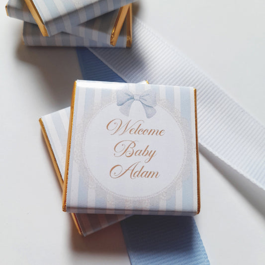personalized chocolate favours for a baby boy, wrapped in pastel blue paper and gold foil.