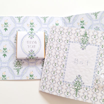 elegant, handmade wedding favours featuring a blue botanical design. Each favour includes chocolate, is tied with a ribbon, and can be personalized with names or dates. They are made in the UK and intended as thank-you gifts for wedding guests.